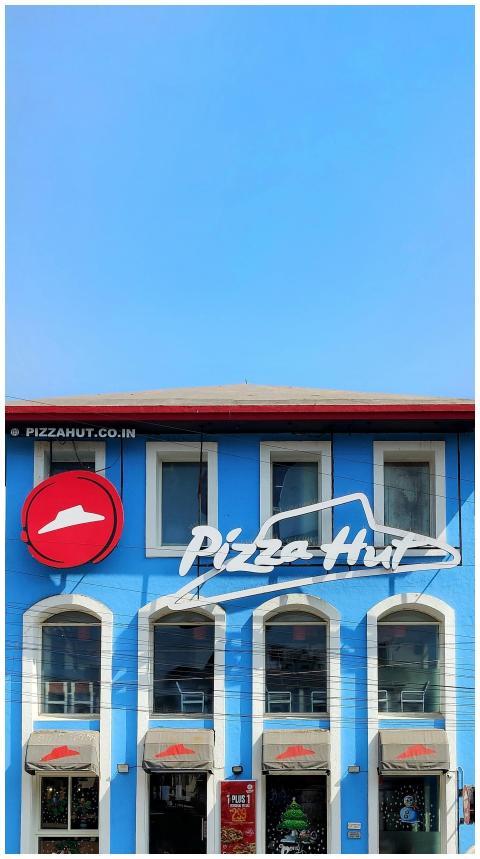 Blue facade of Pizza Hut with clear sky, showcasin