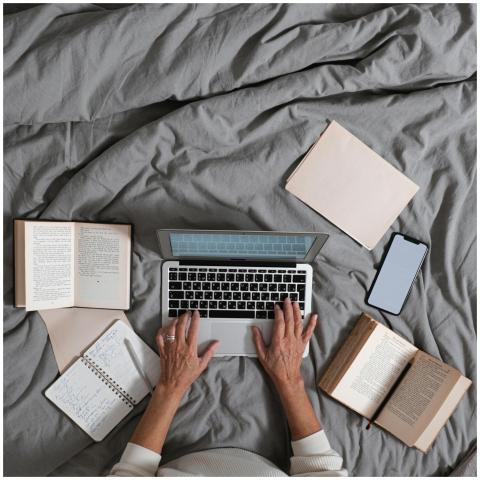 Person typing on laptop surrounded by books and sm