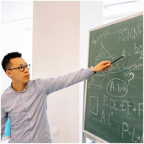 A male teacher points at equations on a blackboard