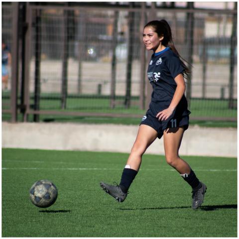 Young female athlete in blue soccer uniform dribbl