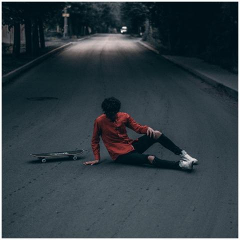 A skateboarder in casual wear sits on a deserted s