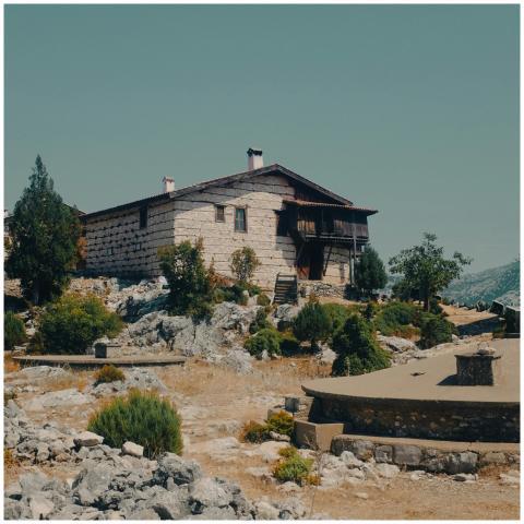 A rustic stone house surrounded by greenery and ro