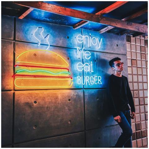 Young man leans against a wall with vibrant neon b