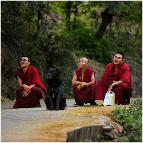 Three smiling monks in red robes sitting outdoors