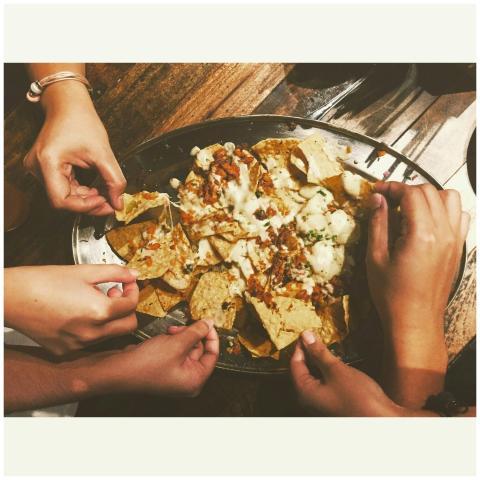Hands reaching for delicious cheesy nachos in Maka