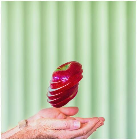 A sliced red apple floating above hands in front o