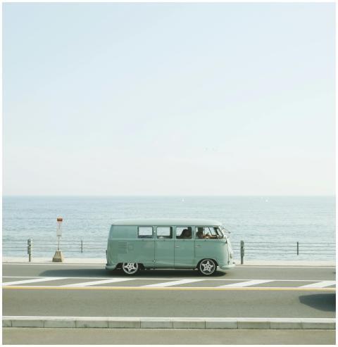 A classic Volkswagen van driving on a seaside road